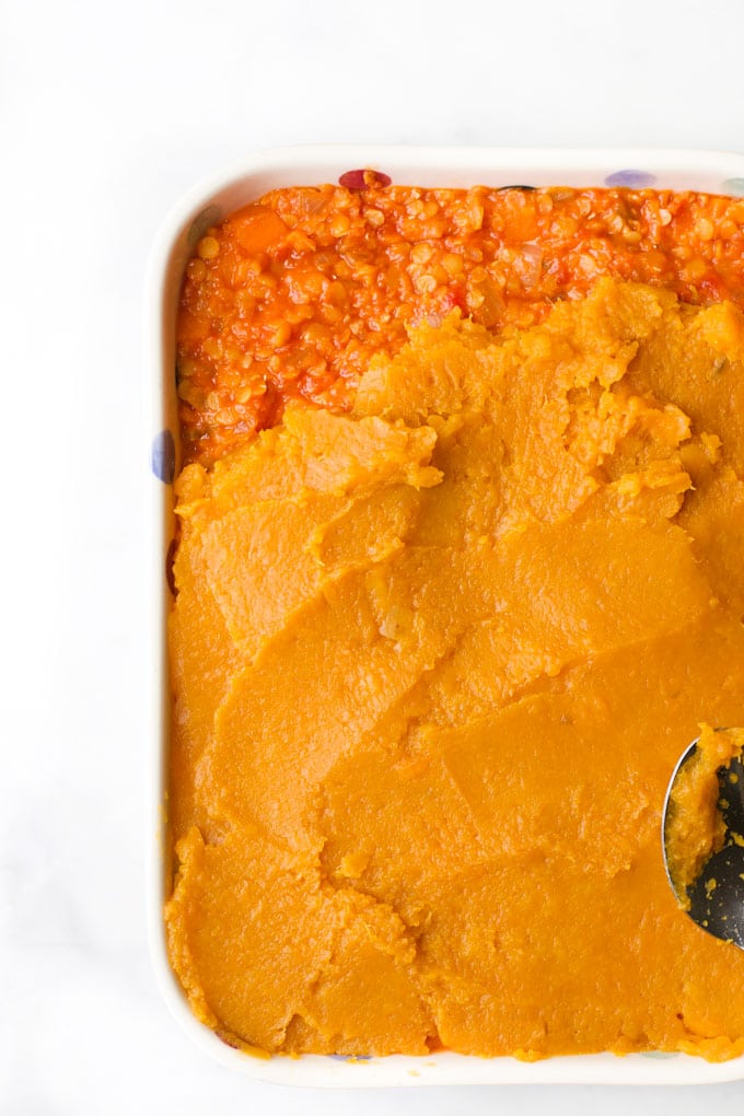Baking Dish Filled with Lentil Mixture and Being Topped With Sweet Potato