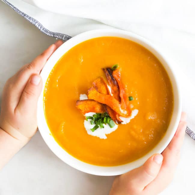 Child Grabbing Bowl of Carrot and Orange Soup