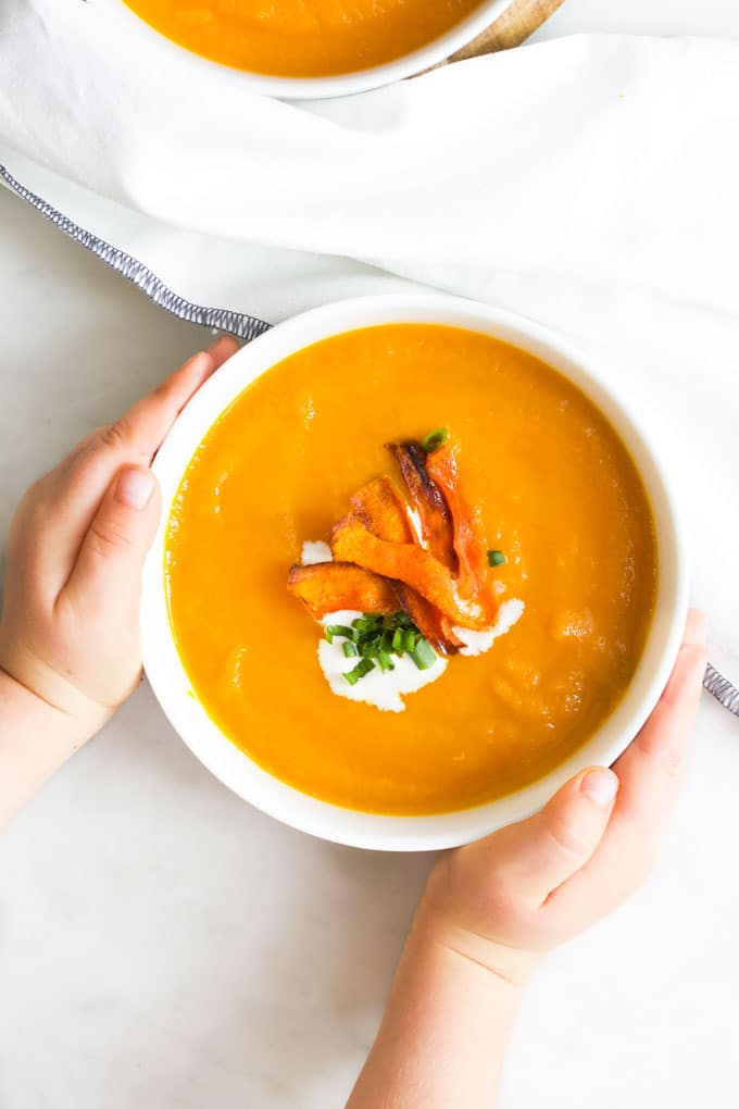 Child Grabbing Bowl of Carrot and Orange Soup