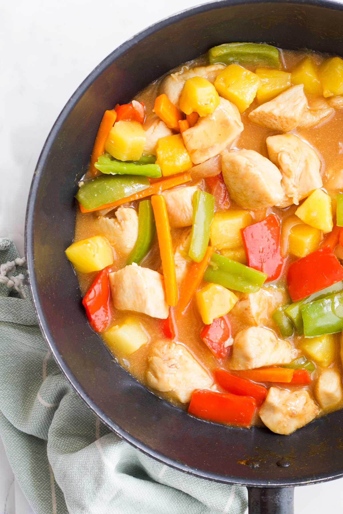 Healthy Sweet and Sour Chicken in Wok with Blue Dish Towel in Background.