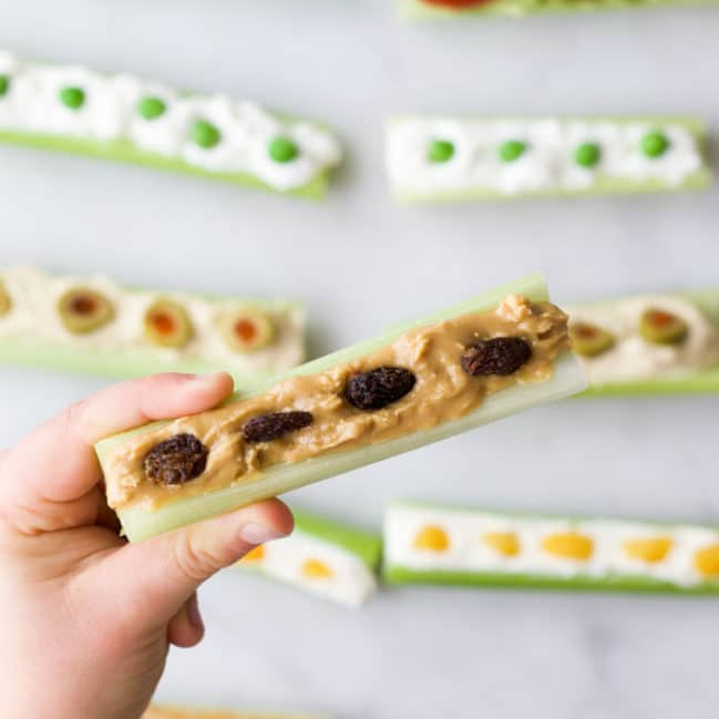 Child Holding Peanut Butter and Raisin Ants on a Log