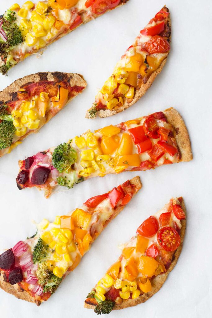 Cooked Pitta Bread Pizza Slices Topped with Cheese and Rows of Colourful Vegetable Pieces