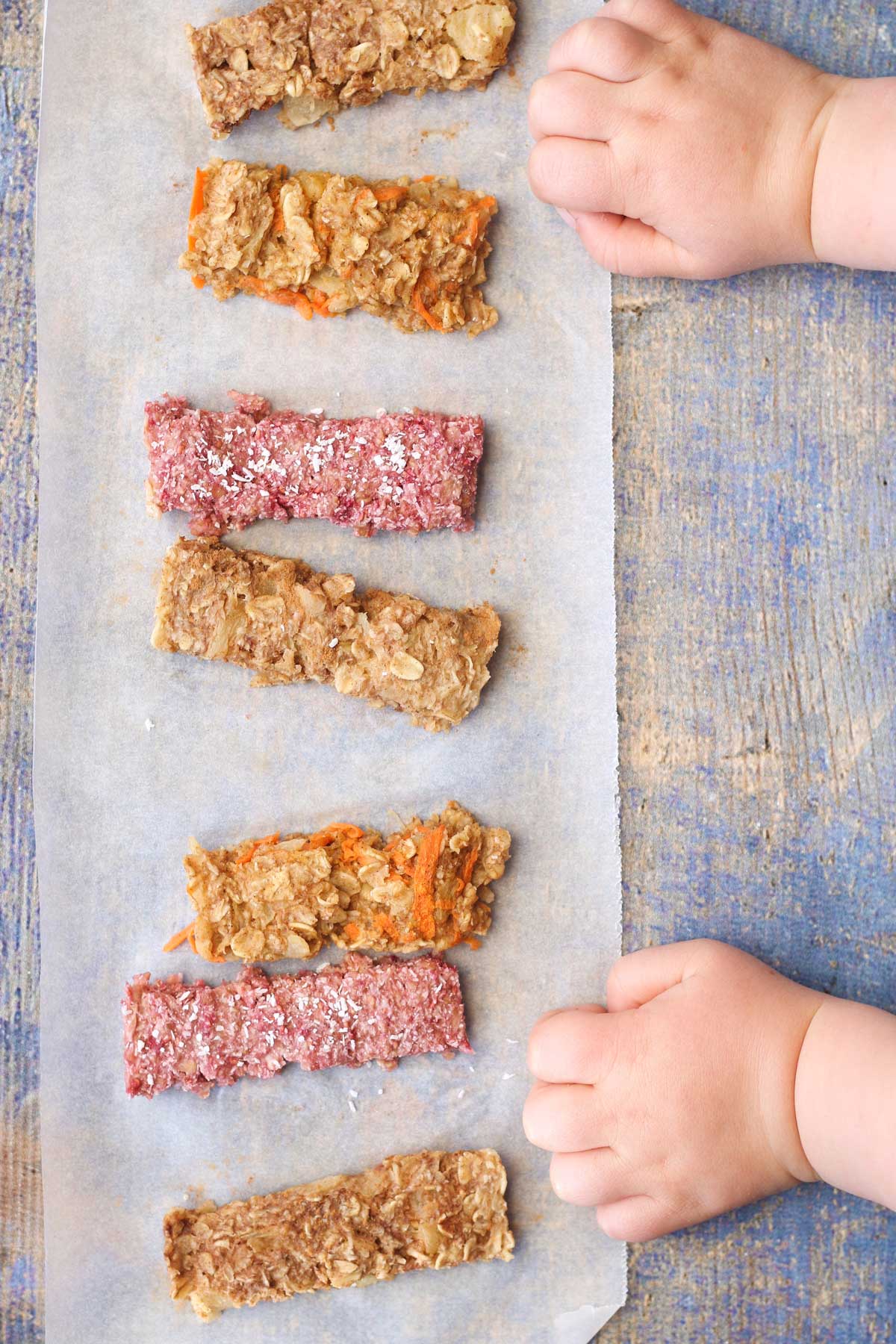 Top Down Shot of Row of Porridge Fingers on Blue Background with Baby Hands Next to Them