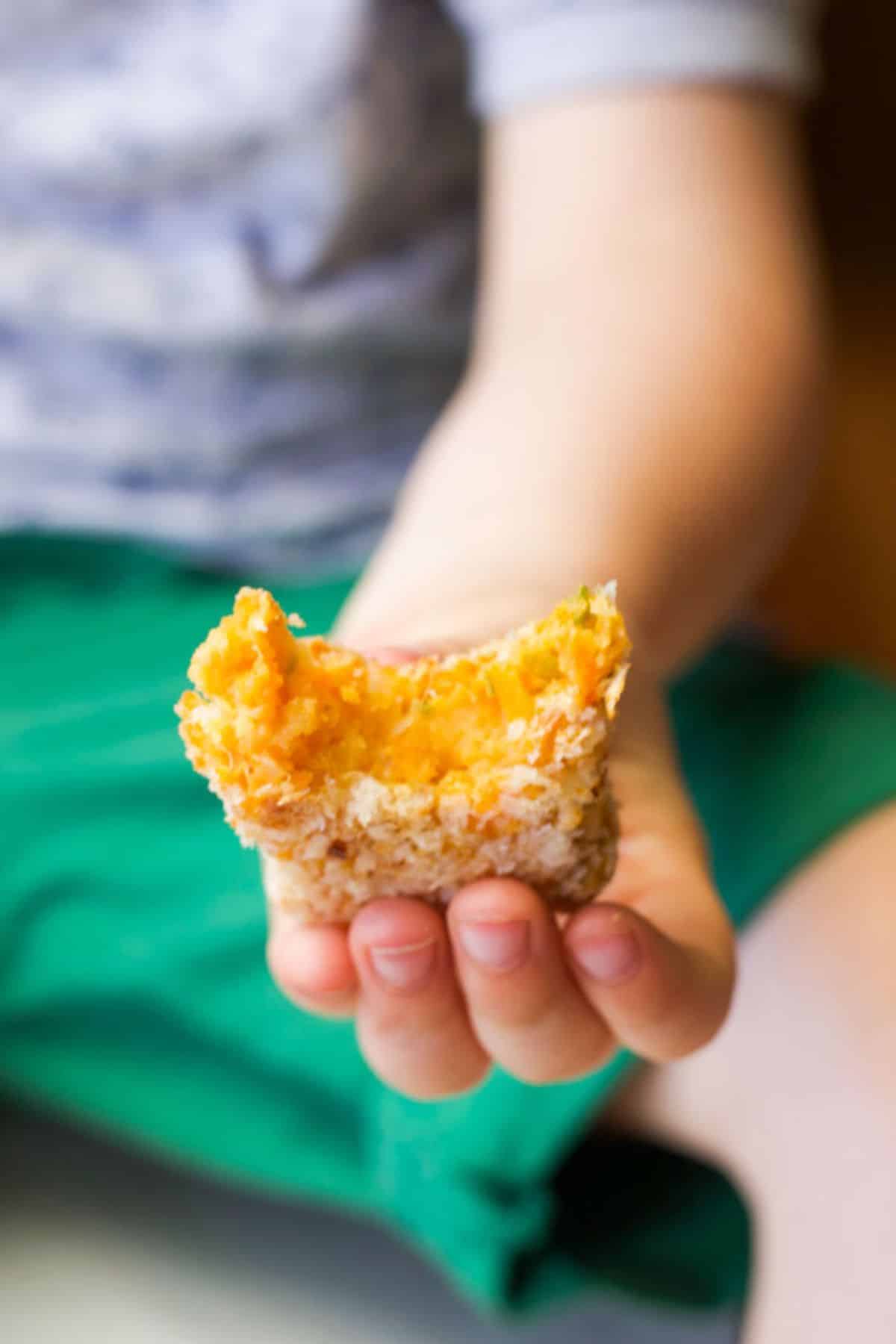 Child Holding a Lentil and Sweet Potato Croquette with Bite Removed.