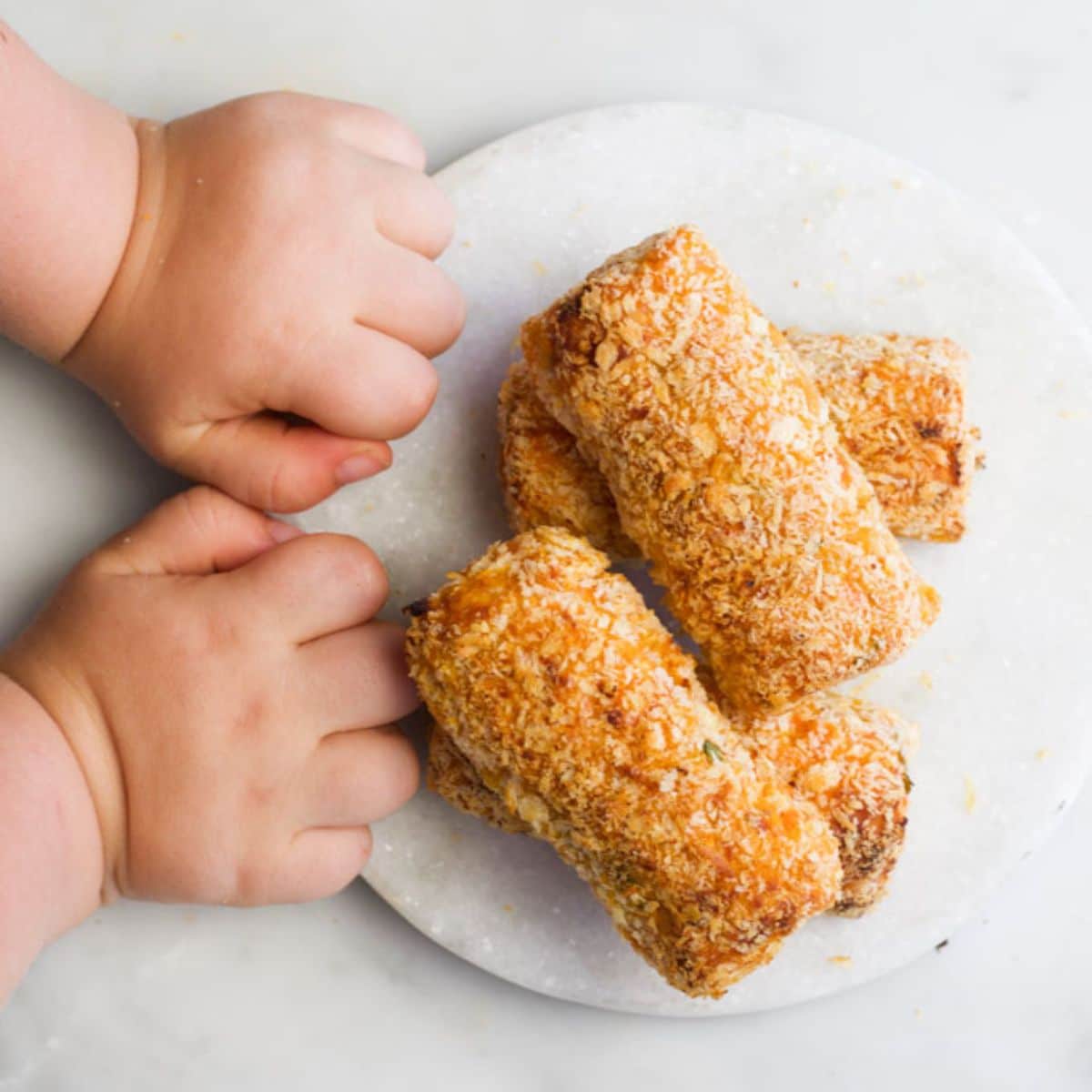 Sweet Potato and Lentil Croquettes on Marble Board with Toddler Hands Next to It.