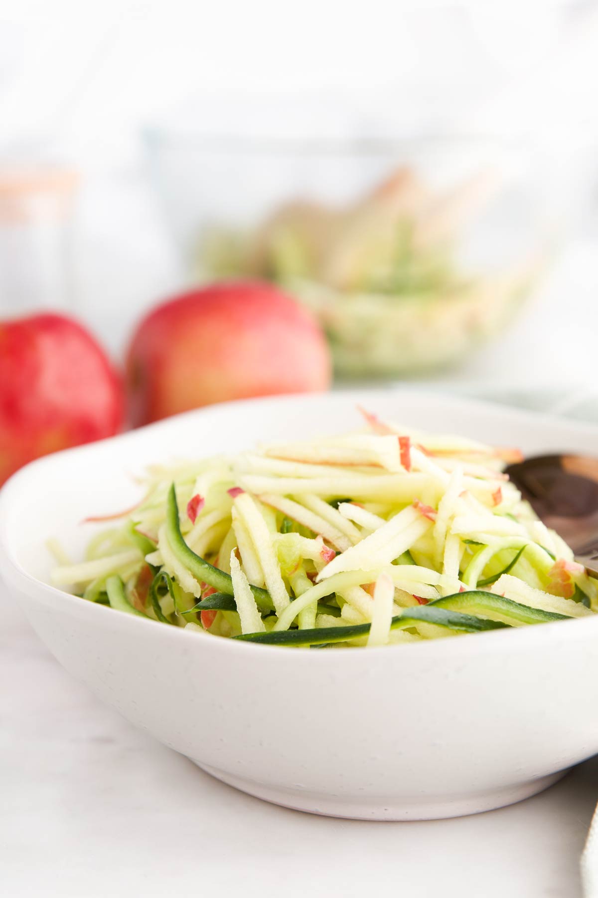 Apple Cucumber Salad in White Serving Bowl with Apples and Larger Bowl of Salad in Background