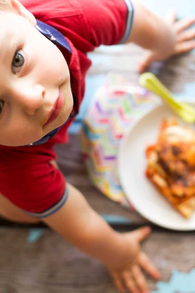 Child Looking Up at Camera with Lentil Lasagne in Background