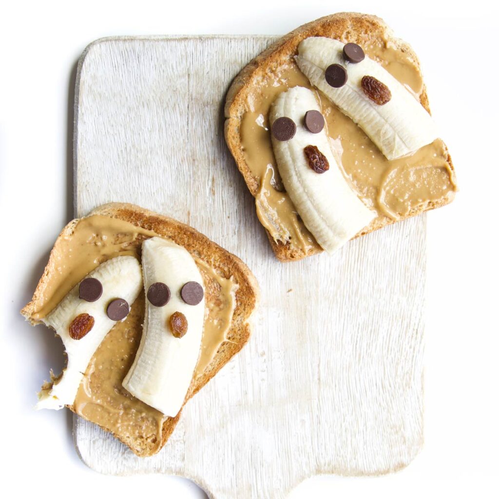 Two Slices of Toast Topped with Peanut Butter and Banana Pieces Made to Look Like Ghosts