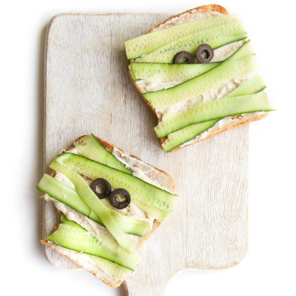 Two Slices of Toast Spread with Hummus with Cucumber Strips to Look Like a Mummy