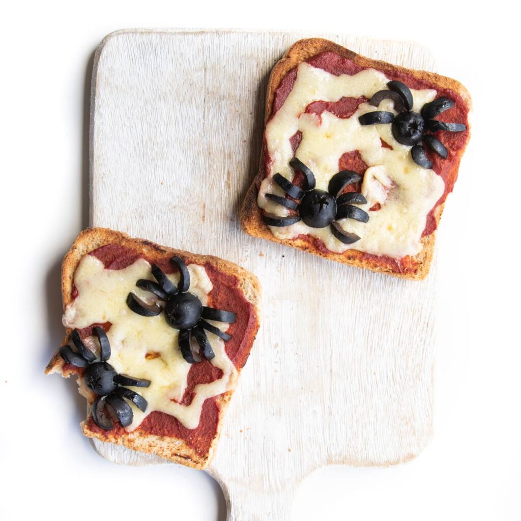 Two Slices of Toast Spread with Pizza Toast and Cheese with Black Olives Cut to Look Like Spiders