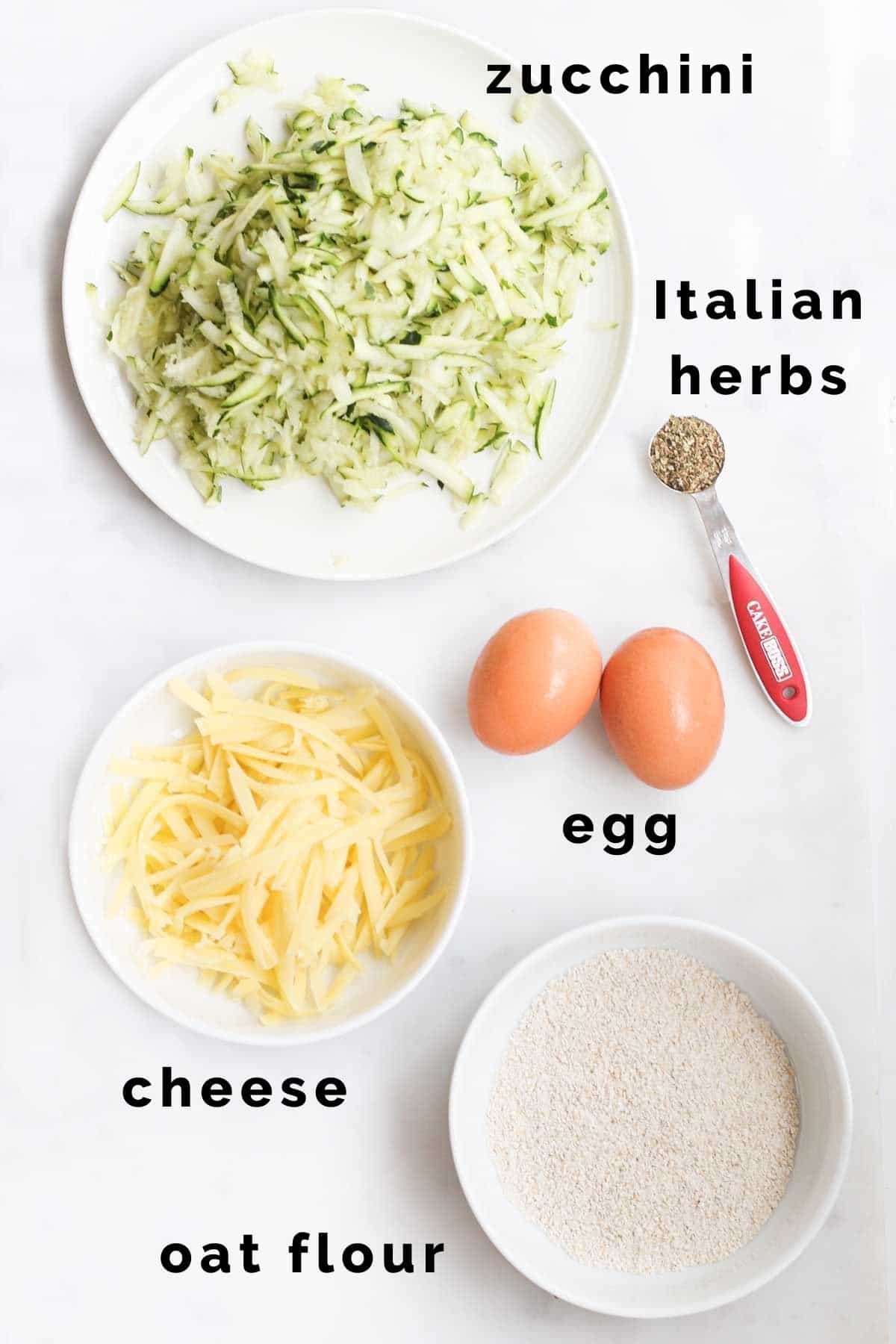 Flat Lay Shot of Ingredients Needed to Make Zucchini Bites (Grated Zucchini, Grated Cheese, Egg Oat Flour, Italian Herbs)