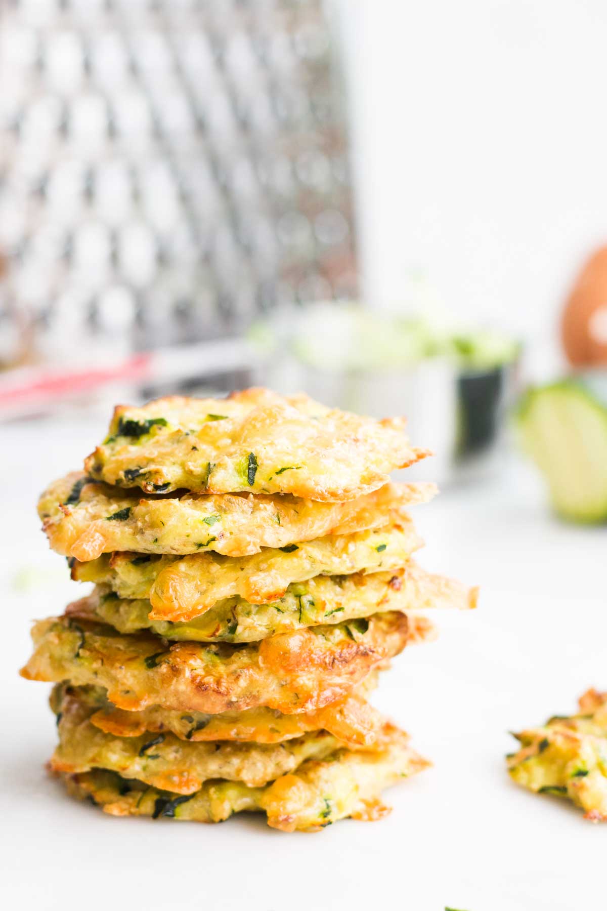 Side Shot of a Stack of Zucchini Bites with Grater and Ingredients in Background