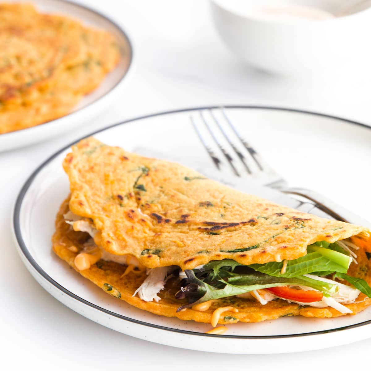Crepe Style Red Lentil Pancake Filled with Salad Folded Over on White Plate.