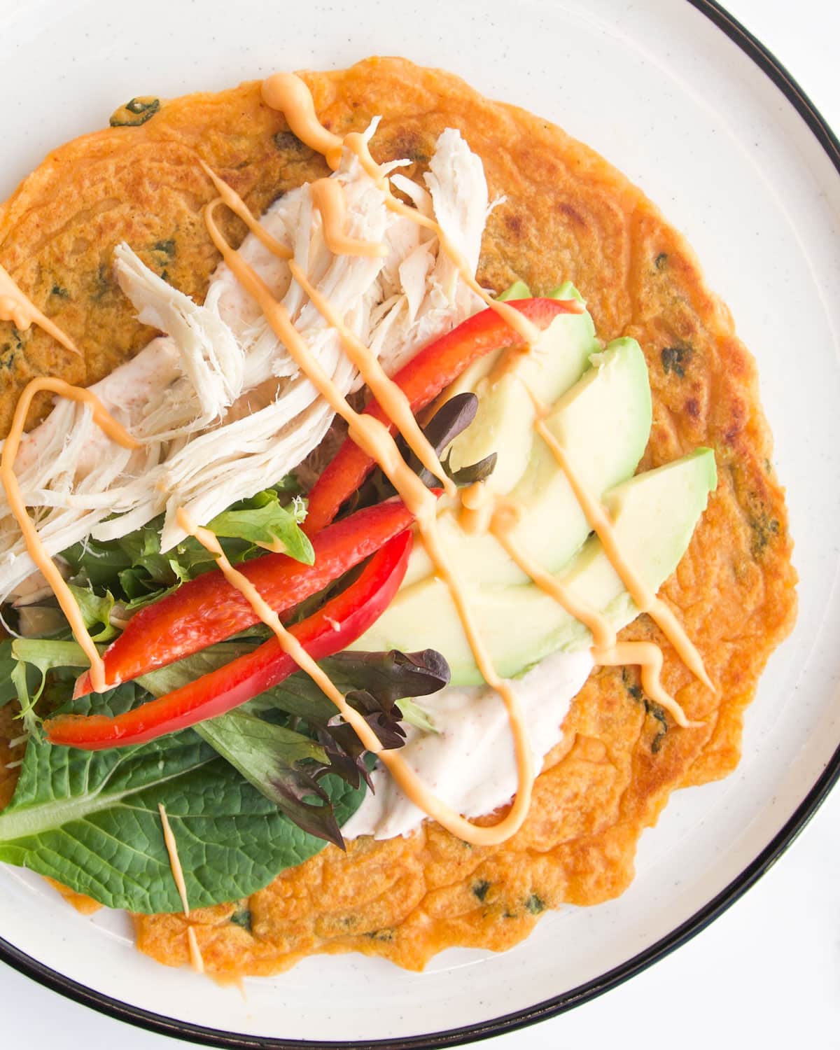 Lentil Pancake on White Plate Topped with Chicken, Salad, avocado and a Yogurt Dip.