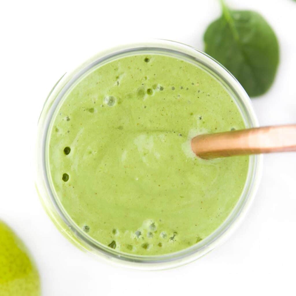 Top Down Shot of Pear Smoothie in Glass with Bronze Straw. Spinach Leave and Pear in Background