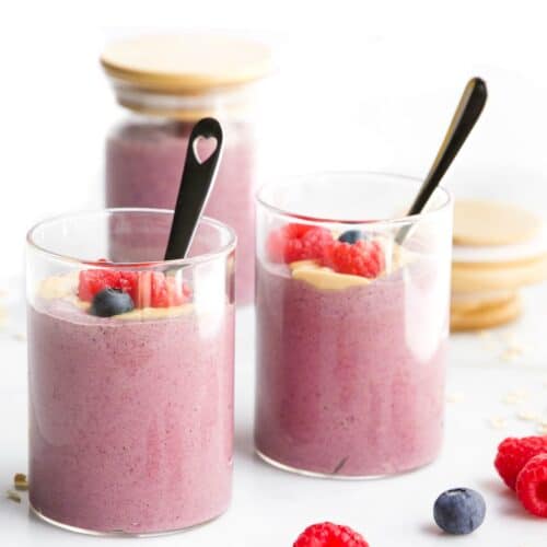 Side Shot of Two Jars of Blended Oats Topped with Berries. Third Jar in Background and Berries Scattered in Foreground