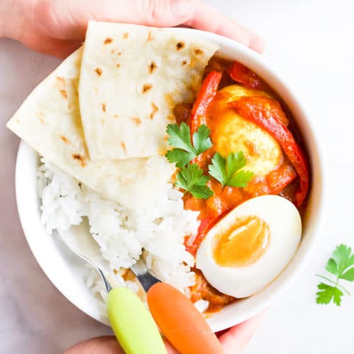 Child Holding Bowl of Egg Curry with Rice and Roti Bread