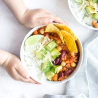 Child Grabbing Bowl of Vegetarian Chilli Topped with Cheese , Avocado and Corn Chips