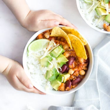 Child Grabbing Bowl of Vegetarian Chilli Topped with Cheese , Avocado and Corn Chips