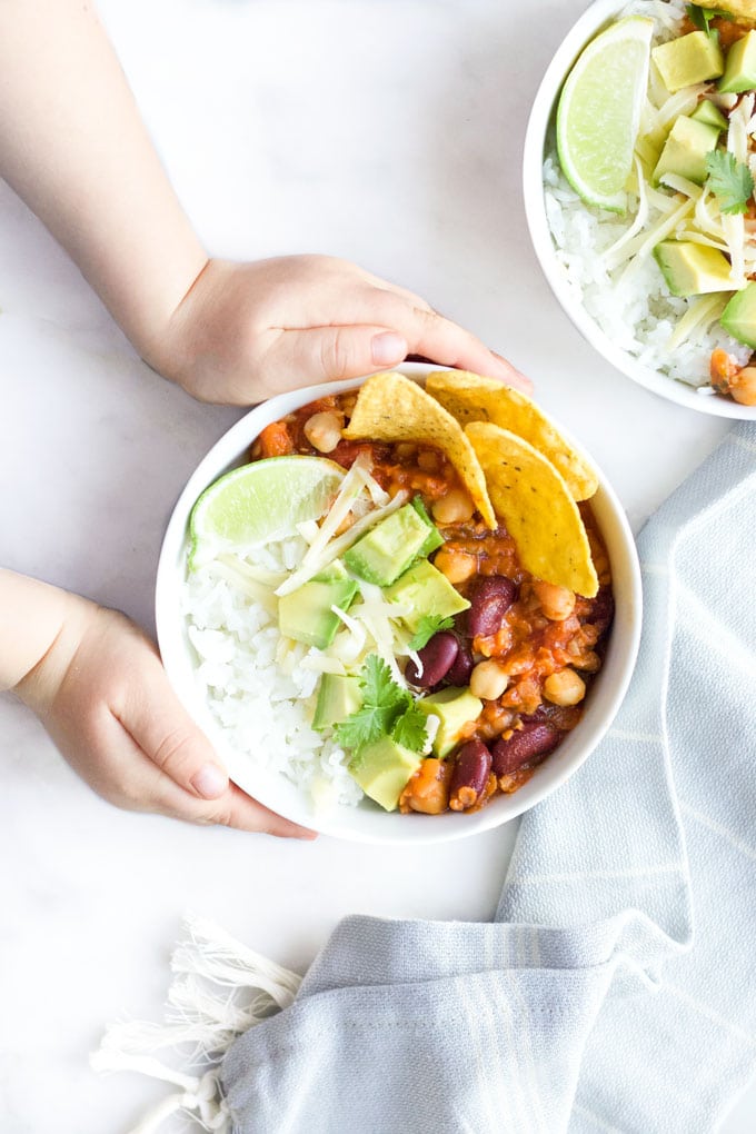 Child Grabbing Bowl of Vegetarian Chilli Topped with Cheese , Avocado and Corn Chips