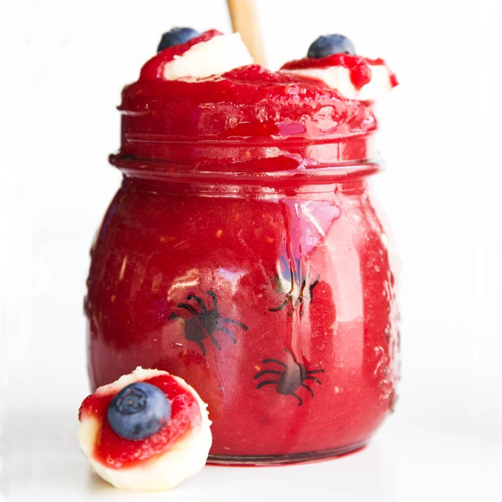 Blood Shot Eye Smoothie. Glass Jar Filled with Deep Red Smoothie topped With Banana Blood Eyes