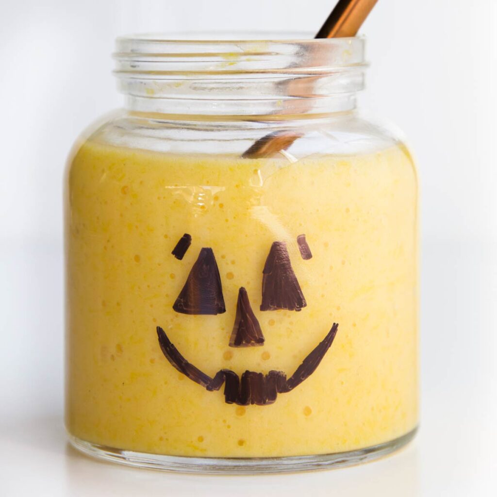 Pumpkin Smoothie. Glass Jar with Pumpkin Face Drawn on Filled with an Orange Smoothie