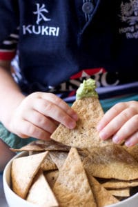Child Holding Baked Tortilla Chip Dipped in Guacamole