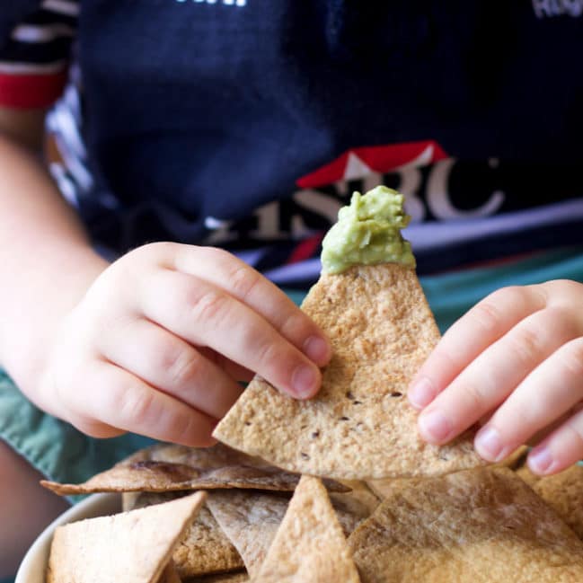 Child Holding Baked Tortilla Chip Dipped in Guacamole