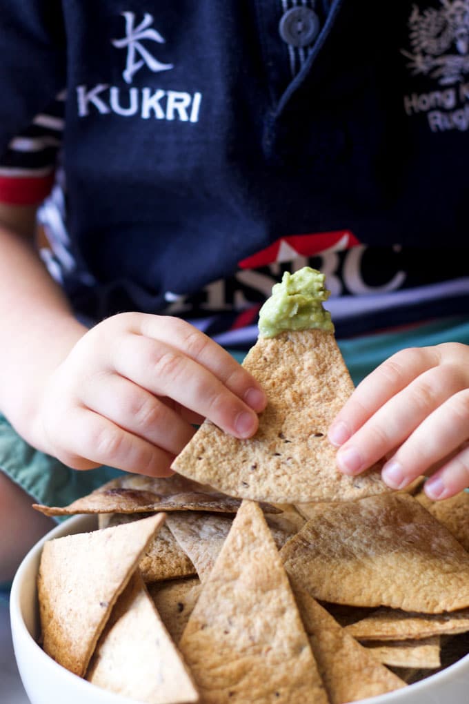 Child Holding Baked Tortilla Chip Dipped in Guacamole