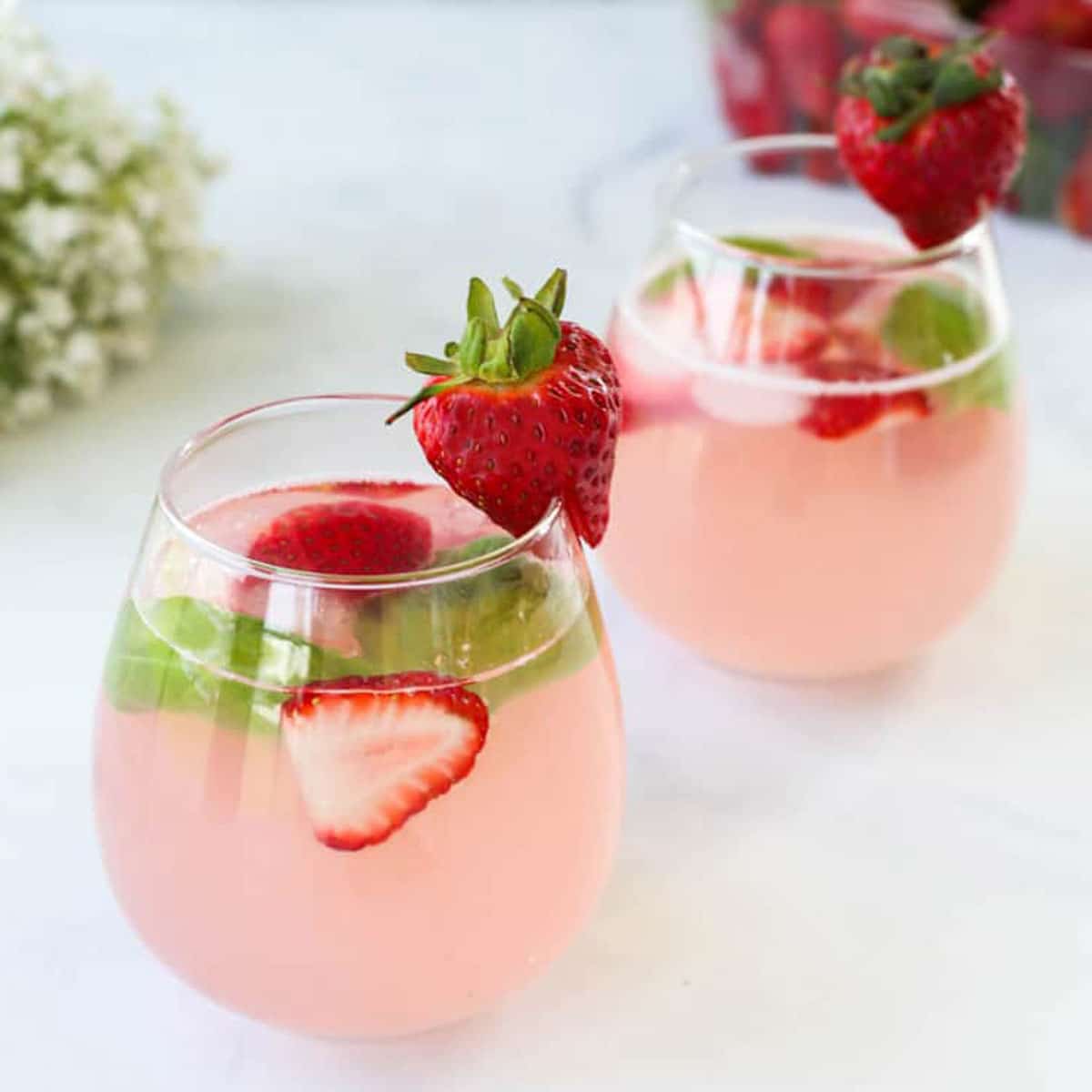 Two Glasses of Strawberry Spritzer Topped with Fresh Strawberries and Basil Leaves.