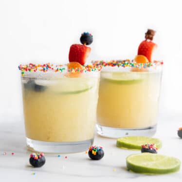 Two Glasses of Fruit Mocktail with Sprinkle Covered Rim and Fruit Kebab Stirrers.
