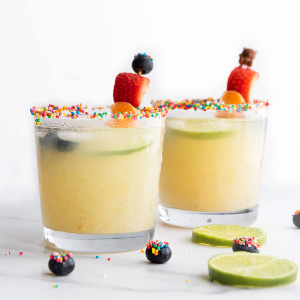 Two Glasses of Fruit Mocktail with Sprinkle Covered Rim and Fruit Kebab Stirrers.