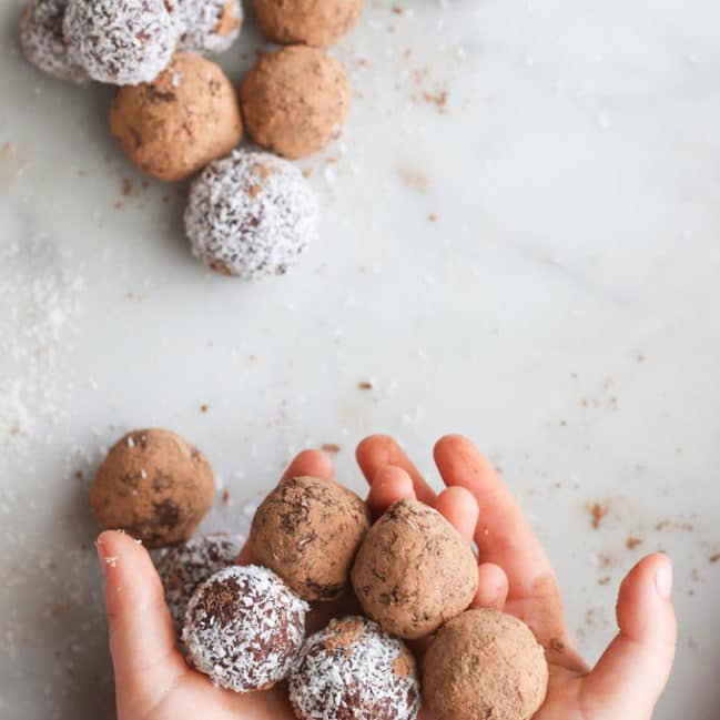 Child holding cherry bliss balls covered in cocao and coconut