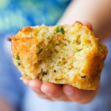 Close Up of Child's Hand Holding Vegetable Savoury Muffin with Bite Removed.