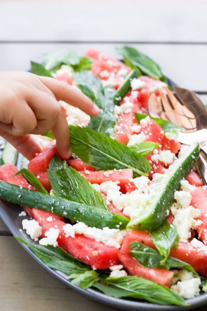 child grabbing piece of watermelon from salad plate