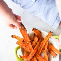 Child Grabbing Roasted Carrot Stick from Bowl