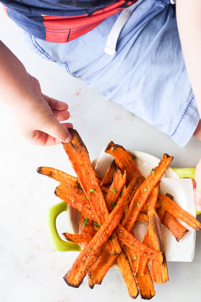 Child Grabbing Roasted Carrot Stick from Bowl