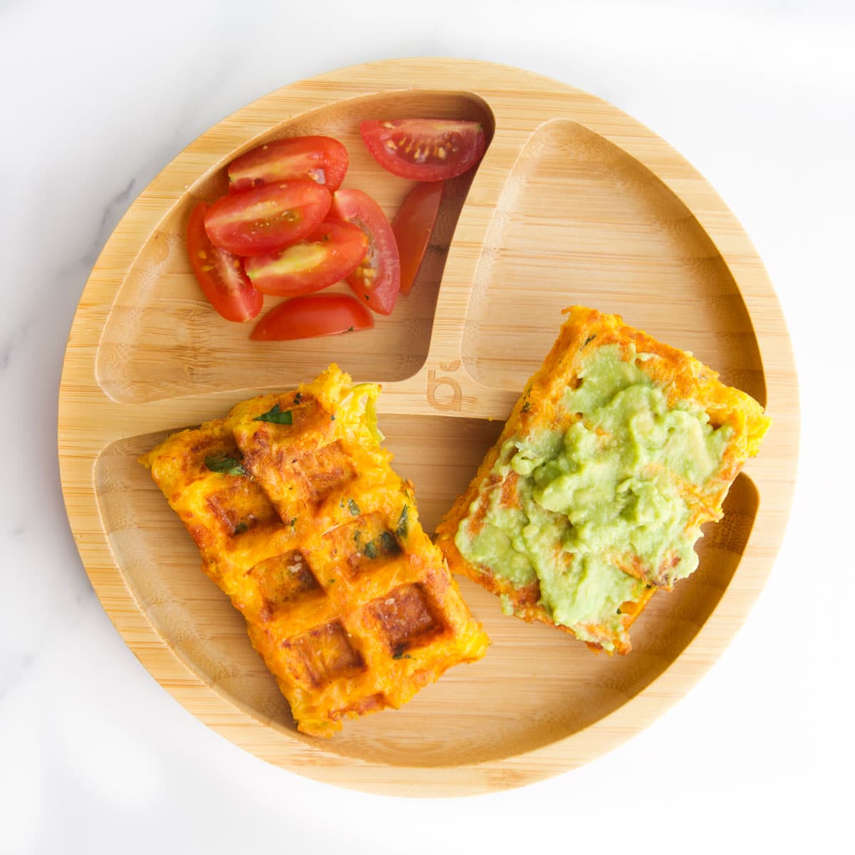 Savoury Waffles Cut into Fingers on Baby Plate Served with Mashed Avocado and Chopped Tomato.