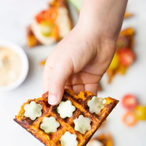 Child's Hand Holding Savoury Waffle with Cucumber Flowers Topping