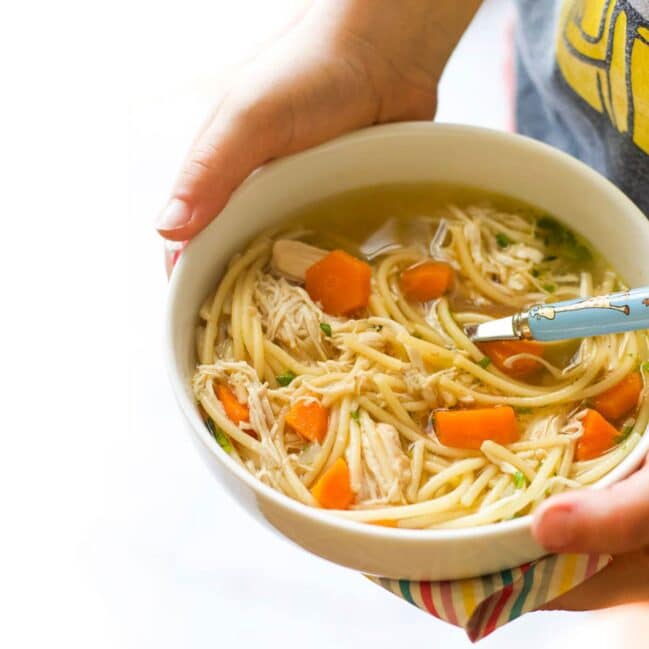 Child Holding a Bowl of Chicken Noodle Soup.
