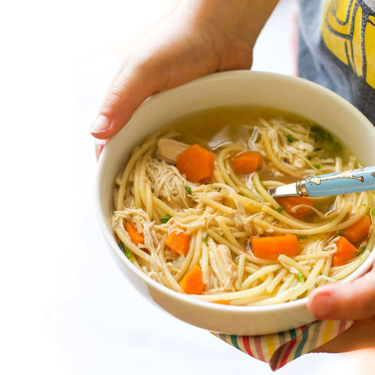 Child Holding a Bowl of Chicken Noodle Soup.