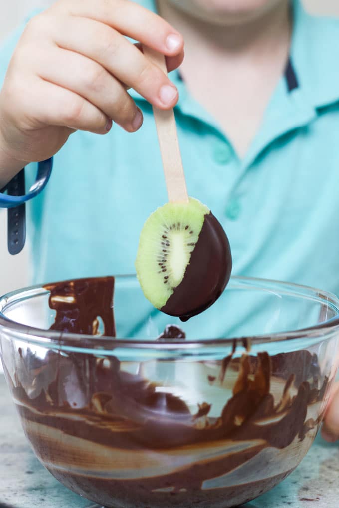 Child Dipping Frozen Kiwi Pop into Melted Chocolate