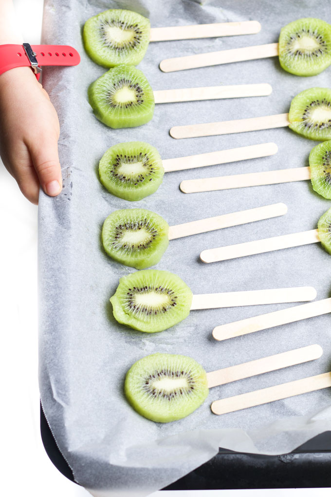 Kiwi Slices on Popsicle Stick Laying on Baking Tray for Freezing