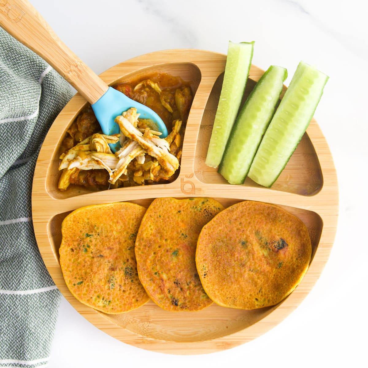 Bamboo Baby Plate with Three Sections. The Main Section Has 3 Chickpea Pancakes, One Section has Chicken Curry and the Last Section Cucumber Sticks.