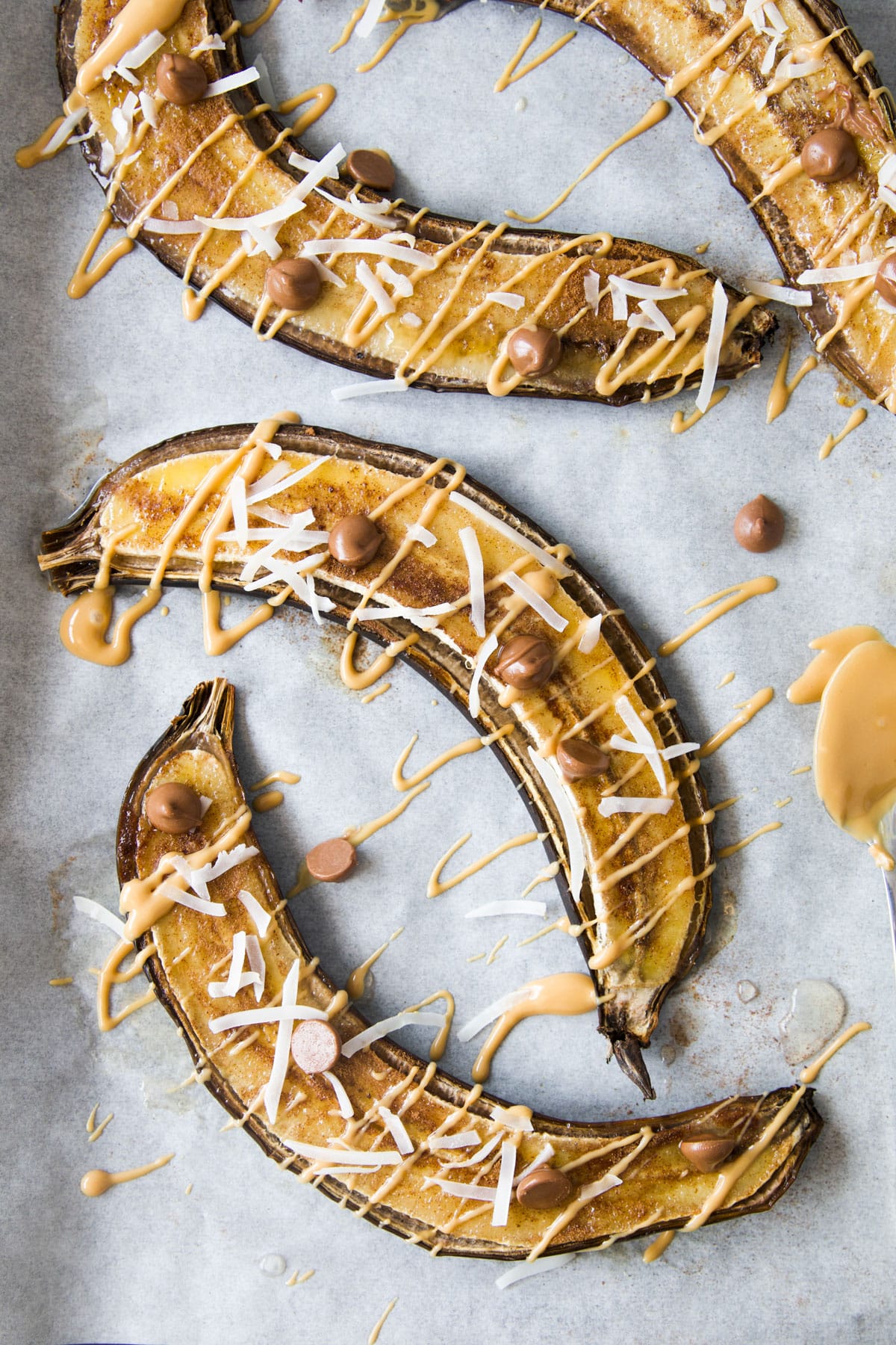 Baked Bananas on Baking Tray Topped with Peanut Butter Drizzle, Coconut and Choc Chips.