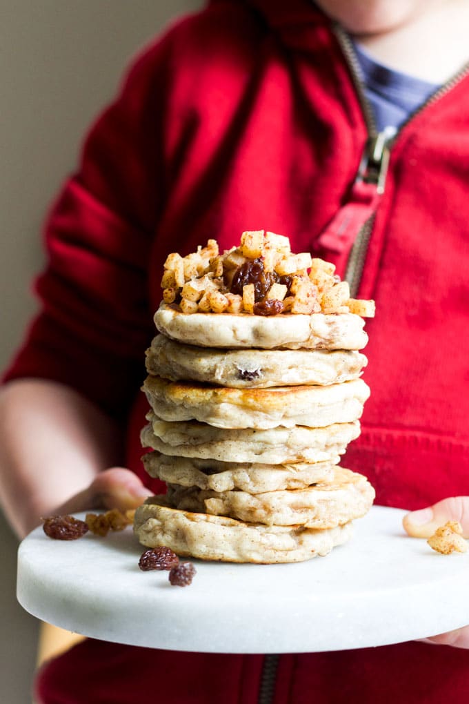 Child Holdin Stack of Apple Pancakes Topped with Cinnamon Apples