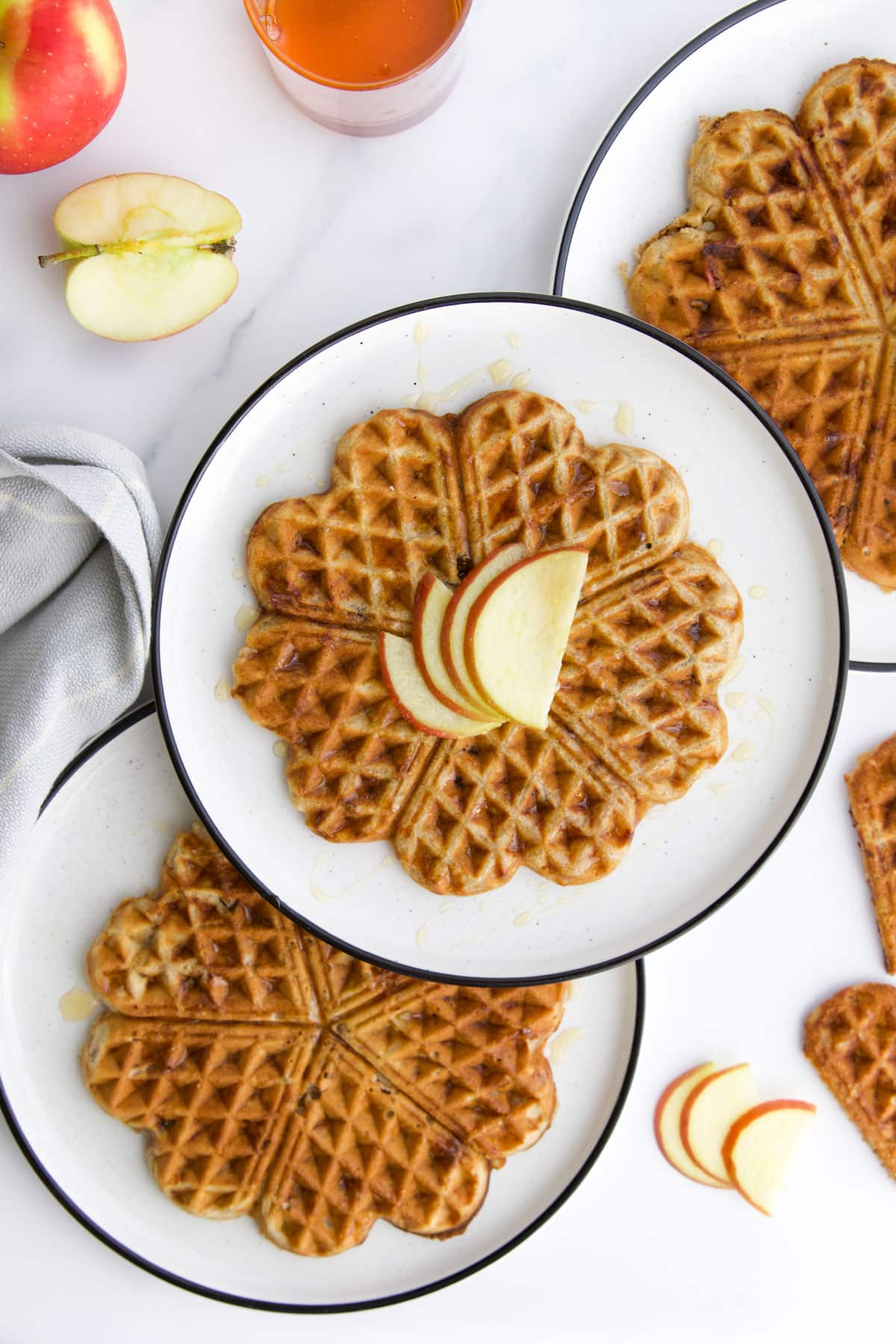 Three Plates Each with An Apple Waffle on Them. Cut Apple and Extra Waffles in Background.