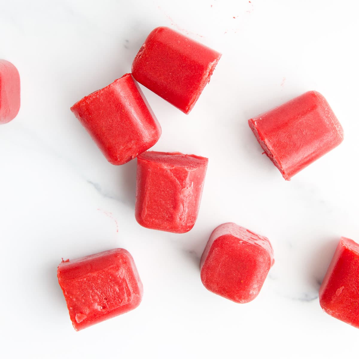 Frozen Strawberry Puree Ice Cubes Scattered on White Surface.