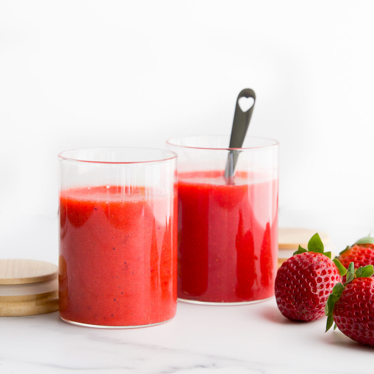 Strawberry Puree in 2 Glass Jars with Strawberries Scattered to the Side. 
