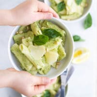 Child Holding Broccoli Pesto Pasta in Bowl